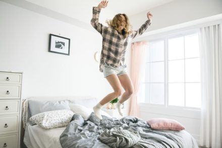 mulher feliz pulando na cama pois tomou a decisão de morar sozinho.